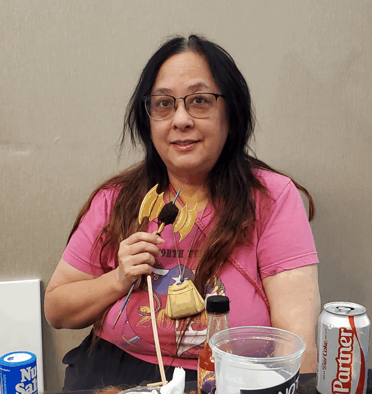 Picture of Manda in a pink NTRPG T-shirt, holding a labrys used for winding fiber.